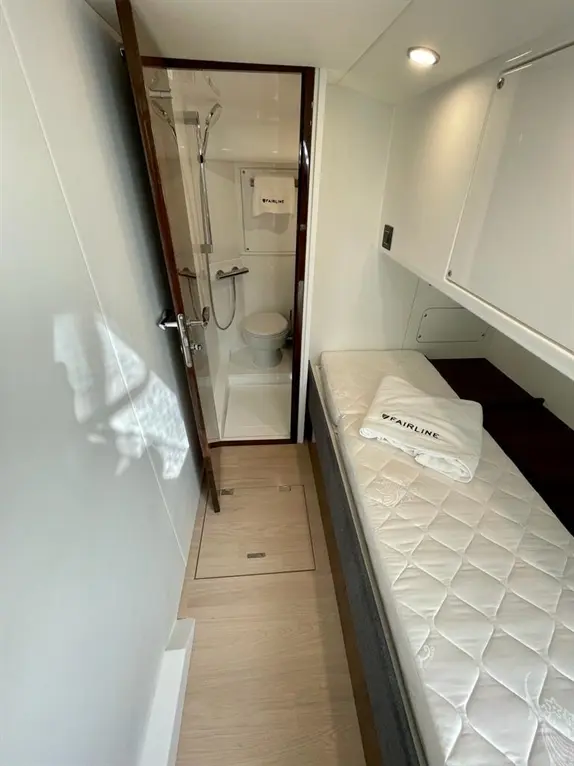 Interior view of a modern boat cabin featuring a shower, toilet, and a single bed with a folded Fairline towel.